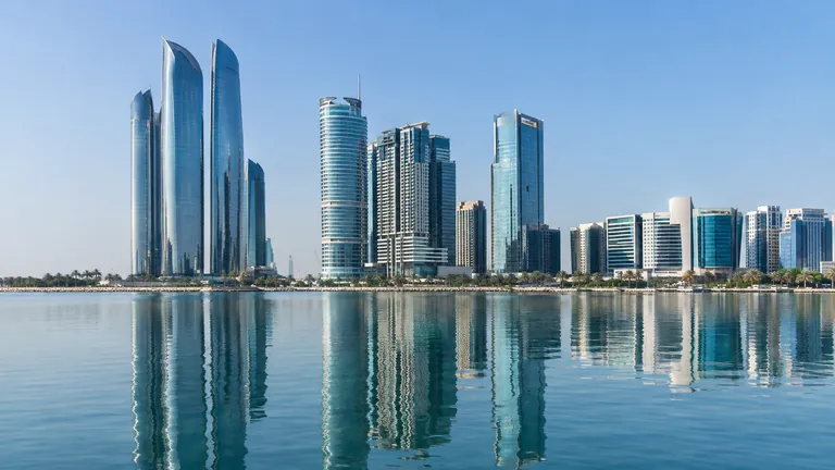 Glass office towers of a financial district on an Abu Dhabi island reflected in calm water