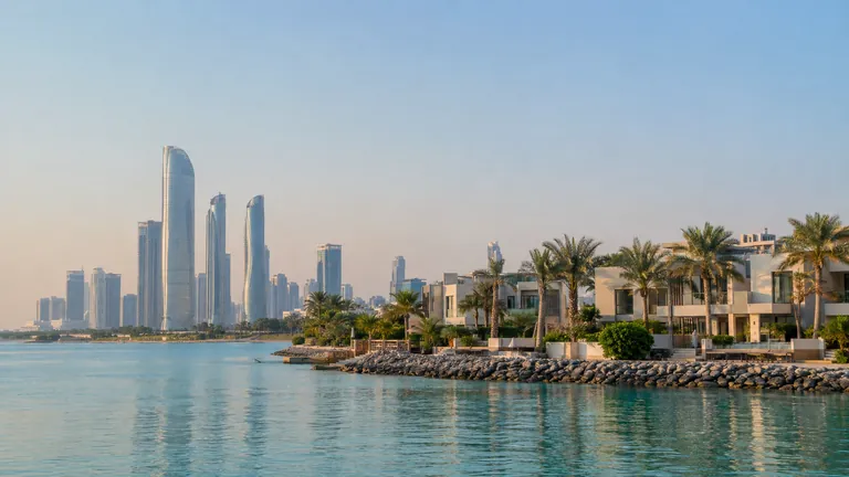 Low-rise waterfront homes and palm trees on an Abu Dhabi island with towers on the horizon