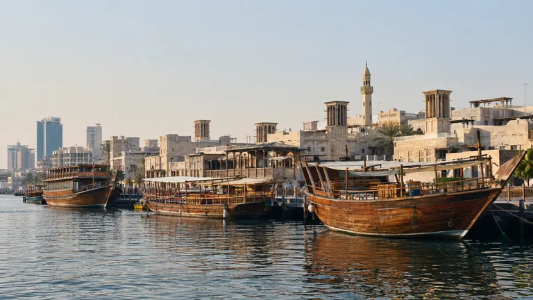 Wooden dhows moored along Dubai Creek with older low-rise buildings behind them