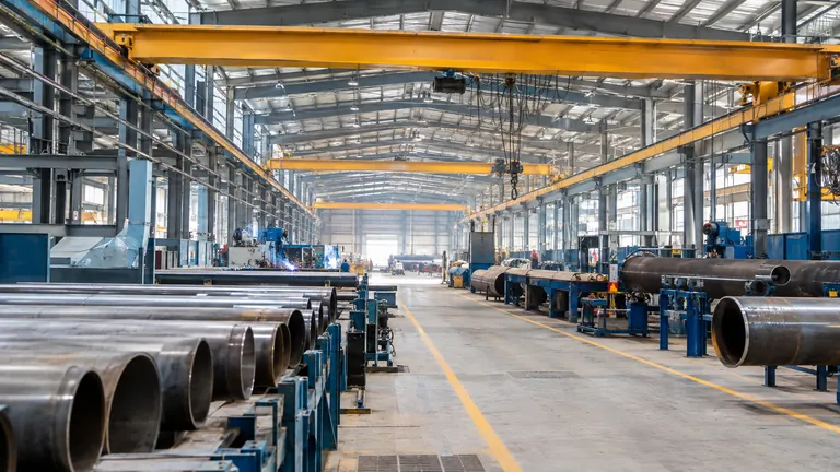 The interior of a large industrial fabrication plant with steel pipes and overhead cranes