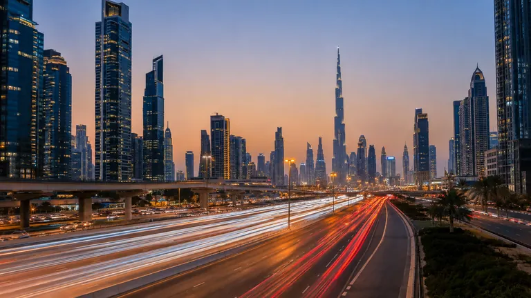 Evening traffic on a wide Dubai highway lined with tall towers, with light trails from cars